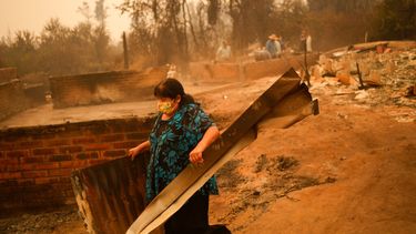 Una mujer remueve escombros en un paisaje devastado por el fuego en Santa Ana, Chile.