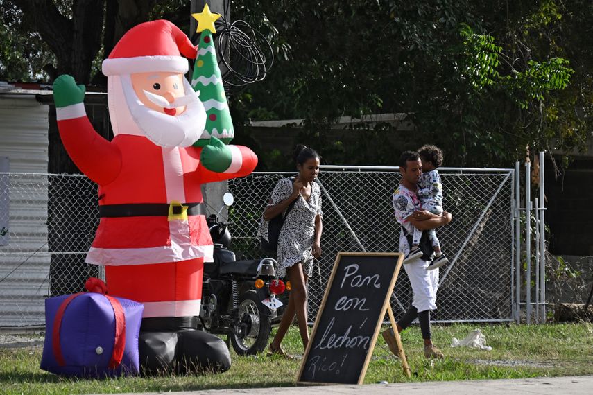 Varias personas pasan junto a un Papá Noel inflable y un cartel que dice Pan y cochinillo. ¡Delicioso! en La Habana, el 23 de diciembre de 2025.&nbsp;