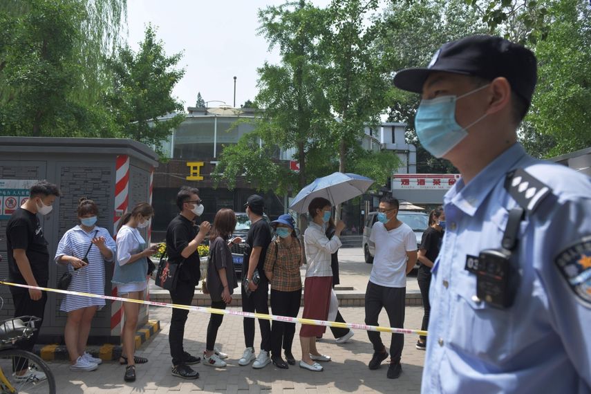 Un polic&iacute;a vigila mientras las personas esperan en la fila para someterse a pruebas de hisopo con coronavirus COVID-19 en una estaci&oacute;n de prueba en Beijing el 28 de junio de 2020.