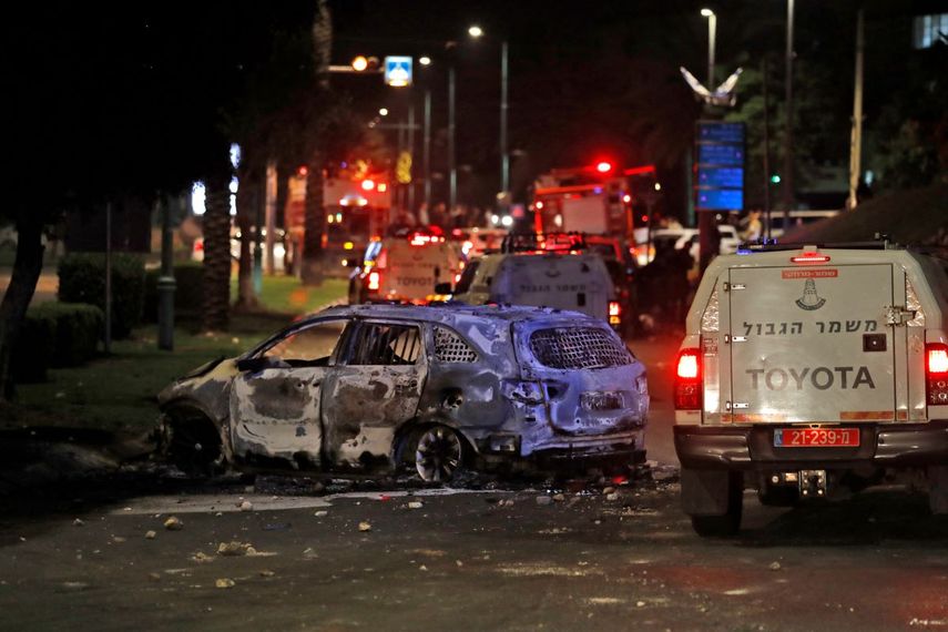 Los vehículos de la policía fronteriza israelí pasan frente a un vehículo quemado extinguido en Lod, cerca de Tel Aviv, el 11 de mayo de 2021, después de que Hamas lanzó cohetes hacia Israel desde la Franja de Gaza controlada por Hamas.