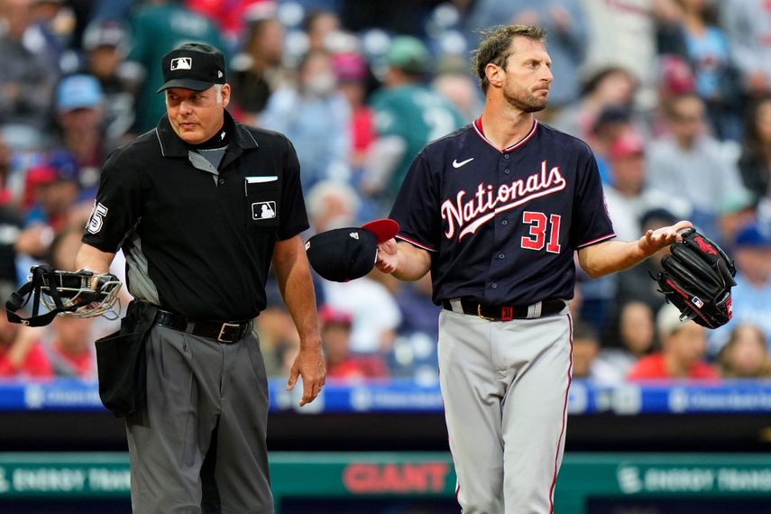 l pitcher de los Nacionales de Washington Max Scherzer (derecha) espera a ser revisado cerca del umpire de plato Tim Timmons tras el primer inning del juego de la MLB que enfrentó a su equipo con los Filis de Filadelfia
