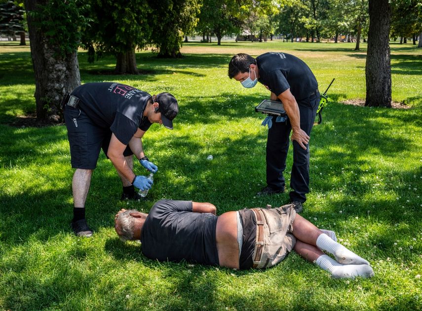 Unos bomberos revisan a un hombre en un parque de Spokane, Washington, el martes 29 de junio de 2021, luego de que la temperatura superó los 37 grados Celsius (100 grados Fahrenheit) en la región a causa de una ola de calor sin precedentes