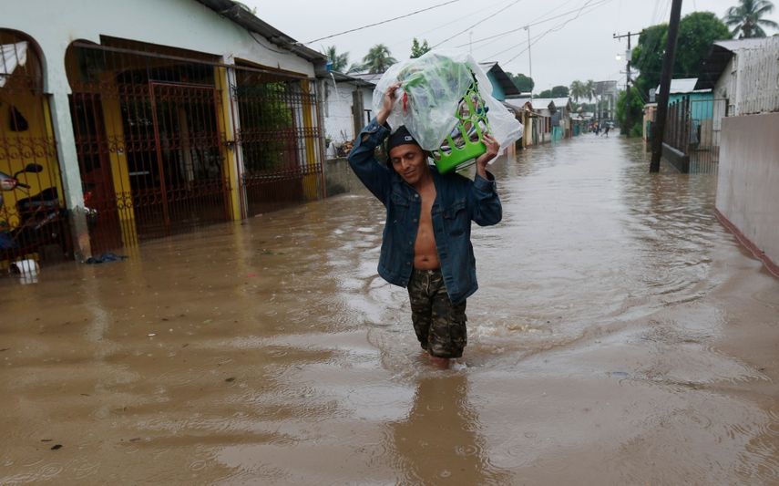 Un hombre camina por una calle anegada, con el agua a la altura de las rodillas, llevando sus pertenencias a cuestas, en San Manuel, Honduras, el 4 de noviembre de 2020
