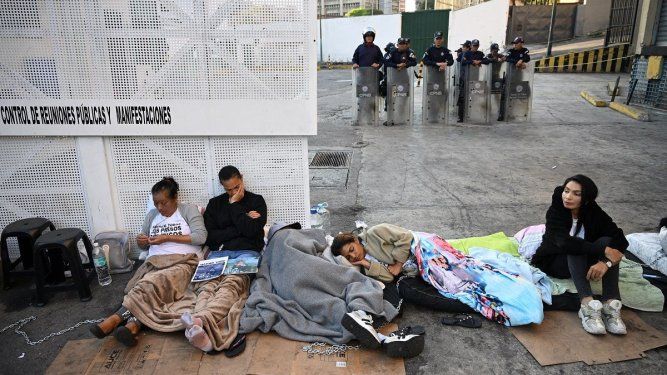 Familiares de presos políticos yacen en el suelo frente a agentes de policía durante una protesta frente a la prisión Zona 7 de la Policía Nacional Bolivariana (PNB) en Caracas el 14 de febrero de 2026.&nbsp;