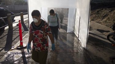 En esta fotografía de archivo del 18 de marzo de 2020, personas con mascarillas protectoras y guantes plásticos caminan por una cámara de descontaminación. Muchos venezolanos se resisten a hacerse la prueba del nuevo coronavirus por temor a ser encerrados en centros obligatorios de aislamiento si se descubre que están infectados. 