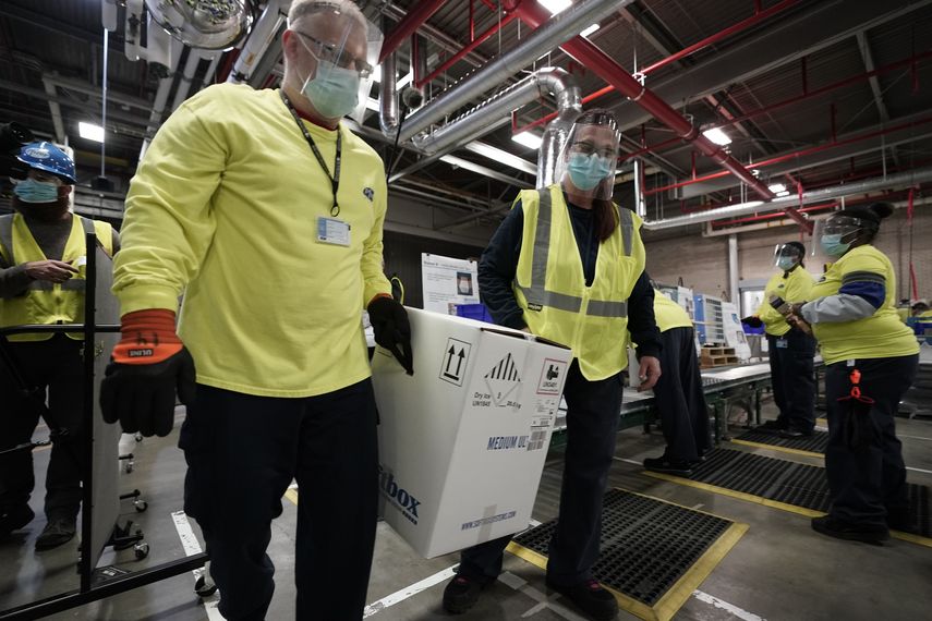 Empleados especializados en cargas de medicamentos trasladan una caja con vacunas.