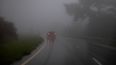 Un automóvil atraviesa una densa niebla y lluvias.