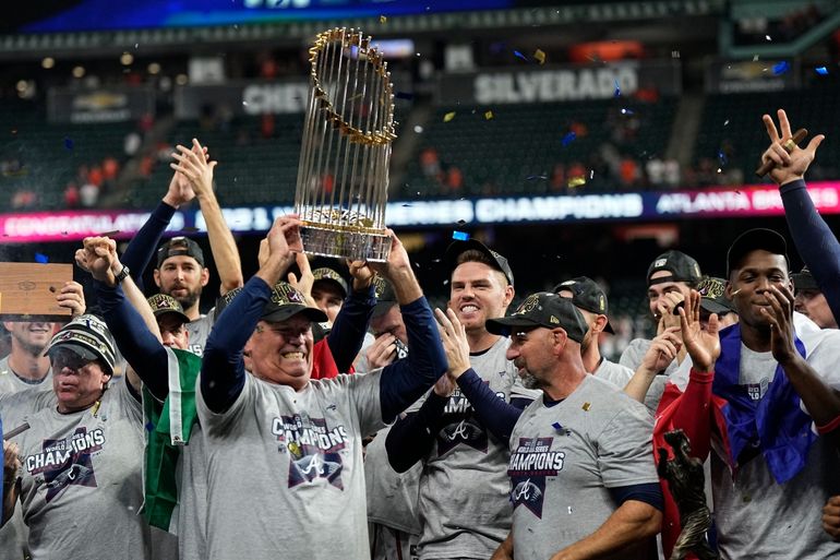 El mánager de los Bravos de Atlanta, Brian Snitker, sostiene el trofeo junto a los peloteros después de ganar la Serie Mundial de béisbol en el Juego 6 contra los Astros de Houston 
