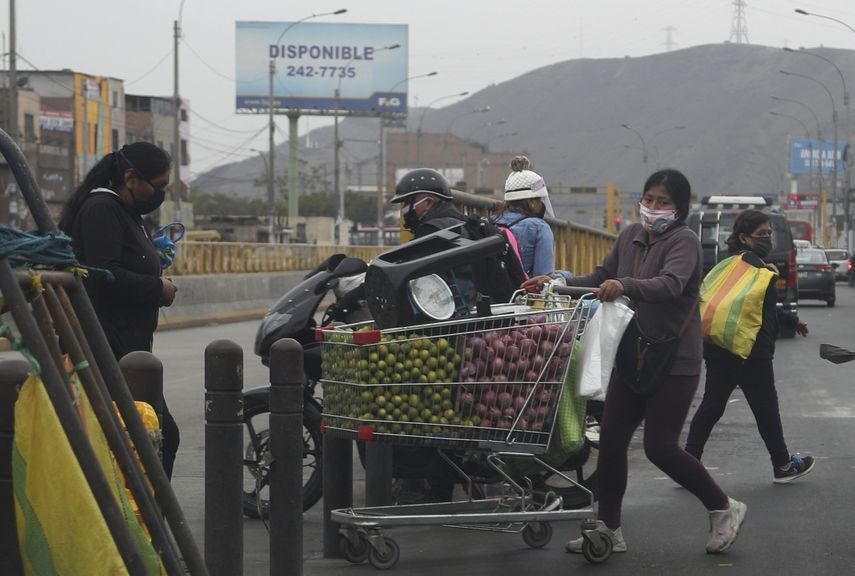 Usando una mascarilla para protegerse del nuevo coronavirus, una mujer joven mueve limones y cebollas en un carrito de compras al mercado en el distrito El Rimac en Lima, Per&uacute;, el mi&eacute;rcoles 27 de mayo de 2020.