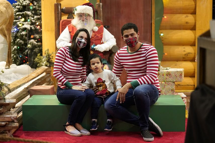 Ariadna y Brian Ferreira usan máscaras protectoras mientras posan con su hijo Enzo con Santa Claus, quien está sentado detrás de una barrera transparente, en Bass Pro Shops, el viernes 20 de noviembre de 2020 en Miami.&nbsp;&nbsp;