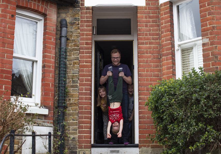 Ben Fox sostiene de las piernas a su hijo Sam mientras Joseph y Stella esp&iacute;an detr&aacute;s suyo en su casa de Berkhamsted, Inglaterra, el 28 de marzo del 2020, durante la cuarentena por el coronavirus.&nbsp;