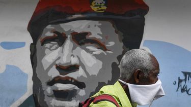 Un hombre que porta una mascarilla improvisada para protegerse del coronavirus camina el domingo 29 de marzo de 2020 junto a un mural del fallecido Hugo Chávez, en Caracas, Venezuela