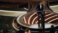 El presentador Chris Rock presenta un premio frente a Jada Pinkett Smith y Will Smith, abajo a la izquierda, luego de que Smith subió al escenario y abofeteó a Rock durante la ceremonia de los premios Óscar, el domingo 27 de marzo de 2022 en el Teatro Dolby en Los Angeles. La policía estaba lista para arrestar al actor.