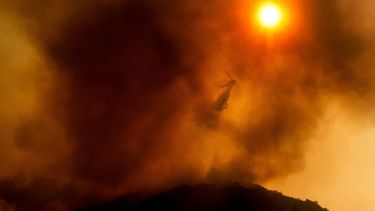 En esta fotografía del lunes 17 de agosto de 2020 un helicóptero arroja agua mientras combate un incendio forestal en Salinas, California
