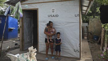 Sandra Ramos, de 22 años, permanece con sus hijos Bryan y Zoy Yamileth Ramos, afuera de una choza improvisada que construyó con ayuda de la Agencia Estadounidense para el Desarrollo Internacional (USAID) a orillas del río Ulúa tras el paso de los huracanes Eta e Iota, en La Lima, departamento de Cortés, Honduras, el 15 de julio de 2022. 