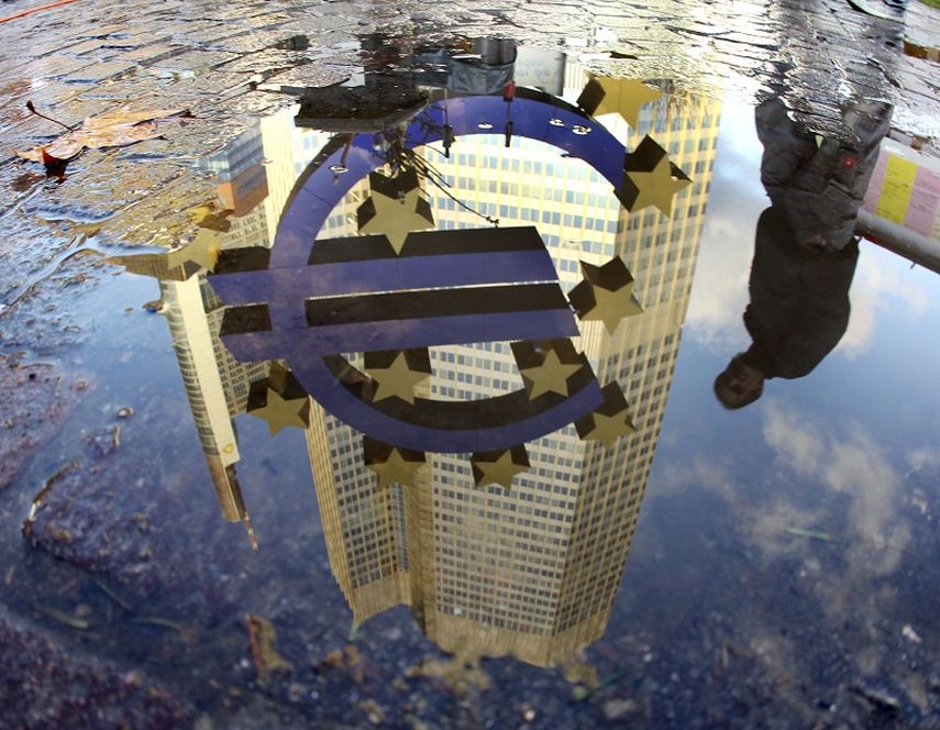 Una persona está reflejada en un charco junto a la escultura del euro frente al Banco Central Europeo en Francfort. (AP)