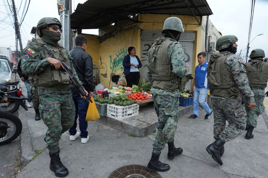 Soldados patrullan el perímetro de la prisión de Inca durante un estado de emergencia mientras un vendedor de alimentos trabaja en la acera en Quito, Ecuador, el martes 9 de enero de 2024, tras la aparente fuga de un poderoso líder de una pandilla de la cárcel.&nbsp;