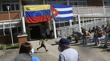 Con el telón de fondo de las banderas nacionales de Venezuela y Cuba, un niño corre mientras la gente espera recibir una inyección de la vacuna cubana Abdala contra COVID-19 en el barrio de Ciudad Tiuna de Caracas, Venezuela, el martes 29 de junio de 2021.&nbsp;