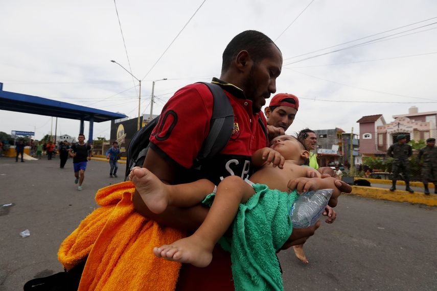 Un padre corre con su hija de un año herida hacia una ambulancia luego de enfrentamientos de migrantes con la Policía de Guatemala.&nbsp;