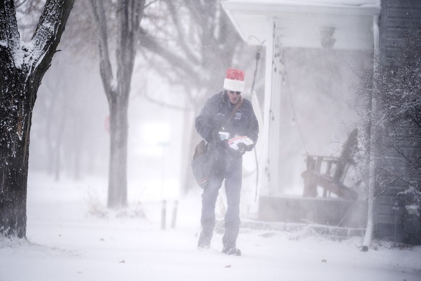 Un cartero con gorro de Santa Claus camina en medio de una tormenta invernal el 23 de diciembre de 2020, en Osseo, Minnesota.