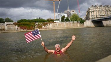 Joel Stratte-McClure, de los Estados Unidos, sostiene una bandera luego de completar un corto nado en el Río Sena, el jueves 4 de julio de 2024, en París.