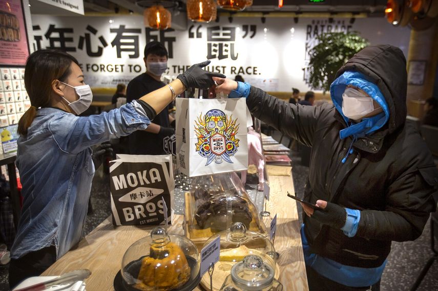 &nbsp; El gerente Chen Tiantian, izquierda, entrega una orden a un repartidor en la cafeter&iacute;a Moka Bros de Beijing, el viernes 14 de febrero de 2020. Como muchos negocios en China, Moka Bros pasa apuros para enfrentar las secuelas del brote de coronavirus que ha infectado a decenas de miles de personas en el mundo.&nbsp;