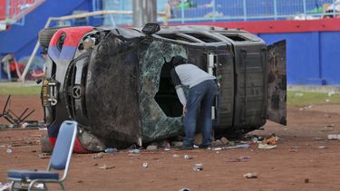 Un oficial de policía vestido de civil inspecciona un automóvil policial destrozado en disturbios de fútbol en el estadio Kanjuruhan en Malang, Java Oriental, Indonesia, el domingo 2 de octubre de 2022.&nbsp;
