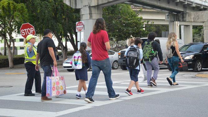 Agente de seguridad gu&iacute;a el paso de peatones en zona escolar.