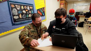 El especialista de la Guardia Nacional de Nuevo México Michael Stockwell, de rodillas mientras ayuda al alumno de secundaria Alamogordo Aiden Cruz con una tarea de geología, en la Escuela Secundaria de Alamogordo, el martes 8 de febrero de 2022 en Alamogordo, Nuevo México.