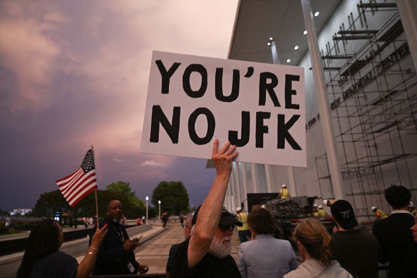 Un hombre sostiene un cartel en señal de protesta mientras la gente observa cómo se retiran los letreros del Centro Conmemorativo Donald J. Trump y John F. Kennedy para las Artes Escénicas en Washington, DC, el 12 de junio de 2026.