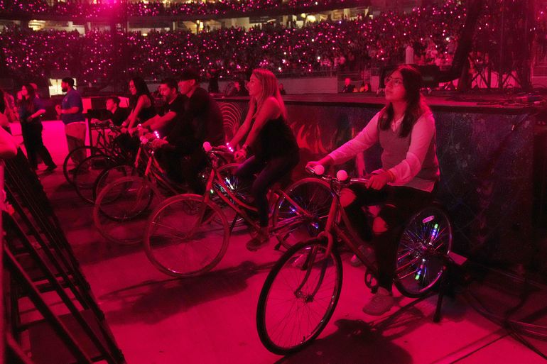 Asistentes montan bicicletas estacionarias durante un concierto de la gira mundial Music of the Spheres de Coldplay el jueves 12 de mayo de 2022 en el State Farm Stadium en Glendale, Arizona.