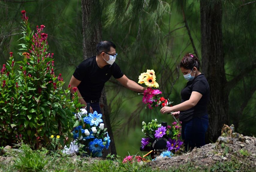 Una pareja lleva flores a la tumba de un familiar que muri&oacute; por COVID-19, en el cementerio de Tegucigalpa, Honduras.&nbsp;