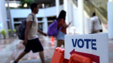 Unas personas caminan junto a un letrero para votar en el primer día de la votación anticipada de las elecciones generales en Miami.&nbsp;