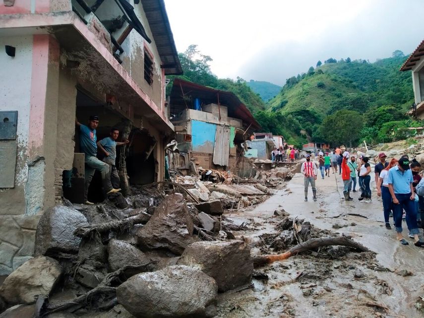 En esta foto proporcionada por la oficina de prensa del gobierno del estado de Mérida, personas caminan por una calle dañada por inundaciones y deslizamientos de tierra provocados por lluvias torrenciales en la zona del Valle del Mocoties del municipio de Tovar en el estado de Mérida, Venezuela.