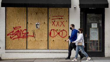 Unas personas con mascarillas caminan frente a una tienda cerrada en Washington D.C., el mi&eacute;rcoles 29 de abril de 2020