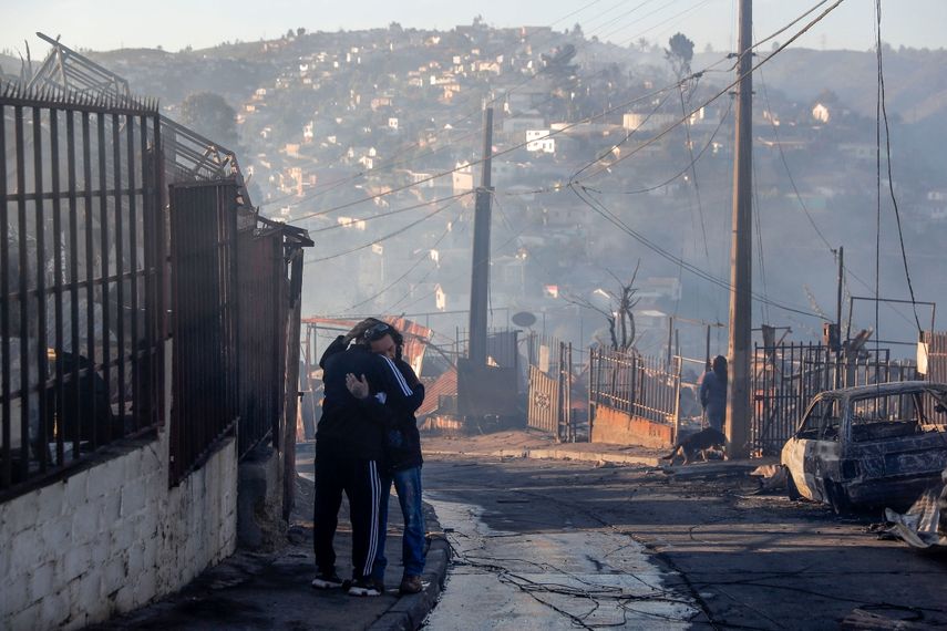 Personas abrazadas en los escombros de casas destruidas por un incendio forestal en los cerros de Viña del Mar, en la región de Valparaíso, Chile, el 23 de diciembre de 2022. Al menos dos personas murieron y unas 400 casas fueron dañadas o destruidas en un incendio que estalló el jueves en el balneario chileno de Viña del Mar, lo que llevó al gobierno a declarar el estado de emergencia.