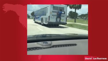 Imagen tomada de un video que muestra a un hombre aferrado a la parte trasera de un autobús en marcha.