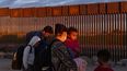 Una familia de migrantes camina se traslada cerca del muro fronterizo entre Estados Unidos y México.