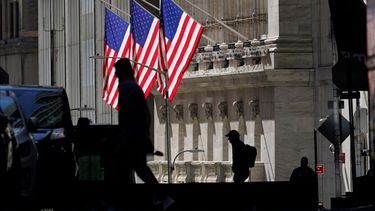 Varias personas caminan frene al edificio financiero de Wall Street.