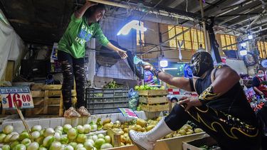 El luchador mexicano Ciclonico le da una m&aacute;scara a una mujer mientras hace campa&ntilde;a para promover su uso en un mercado en Xochimilco, Ciudad de M&eacute;xico, el 28 de agosto de 2020, en medio de la nueva pandemia de coronavirus.