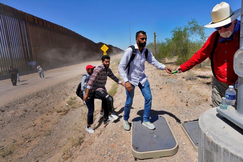 El maestro jubilado Tom Wingo, de Samaritanos Sin Fronteras, a la derecha, entrega bocadillos y botellas de agua a un grupo de inmigrantes que dicen ser de la India y cruzaron el muro fronterizo, 29 de agosto de 2023.