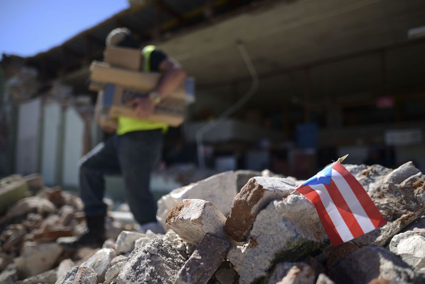 Una bandera de Puerto Rico se ve colocada entre los escombros, mientras los propietarios y familiares retiran suministros de la ferretería Ely Mer Mar, parcialmente derruida tras un terremoto en Guanica, Puerto Rico, el martes 7 de enero de 2020.