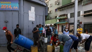 Personas usan mascarillas y pañuelos como medida preventiva contra la pandemia mundial de coronavirus COVID-19, mientras recolectan agua de una tubería&nbsp;en una calle en Caracas, Venezuela, el 21 de marzo de 2020.