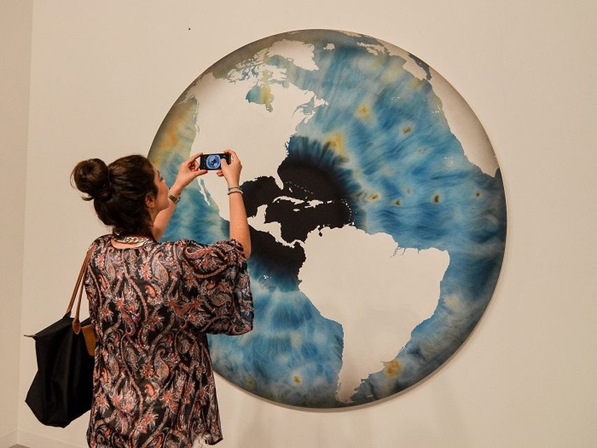 Una amante del arte toma una foto de una obra que muestra el globo del mundo durante la inauguración Art Basel en Miami Beach. (EFE)