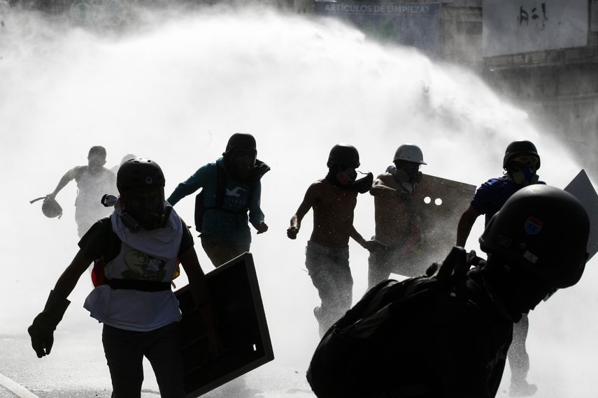 Jóvenes corren al chorro que lanza la Guardia Nacional desde un vehículo antimotines.&nbsp;