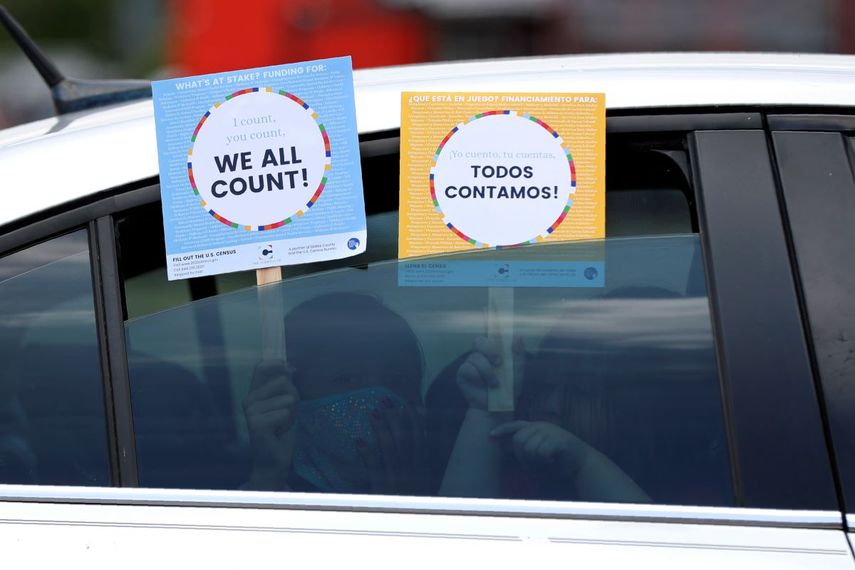 Dos personas dentro de un auto muestran anuncios a favor del censo en EEUU.