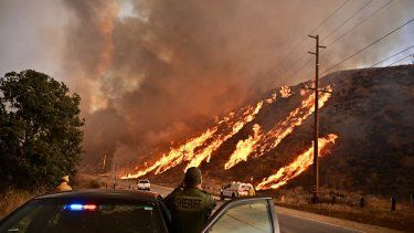 Un alguacil observa cómo las llamas suben por la colina mientras la columna de humo del incendio Hughes llena el cielo en Castaic, un barrio del noroeste de Los Ángeles, California, el 22 de enero de 2025. Un nuevo incendio forestal estalló al norte de Los Ángeles el 22 de enero, creciendo en tamaño y provocando miles de órdenes de evacuación en una región que ya se tambaleaba por los efectos de enormes incendios.