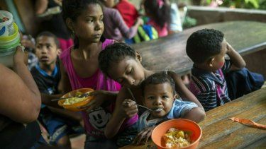 Franyelis, de 8 años de edad, da de comer a su hermanito Joneiber mientras la madre de ambos, Francibel Contreras sostiene un plato con huevos revueltos y arroz en una cocina del barrio de Petare, en Caracas, Venezuela.