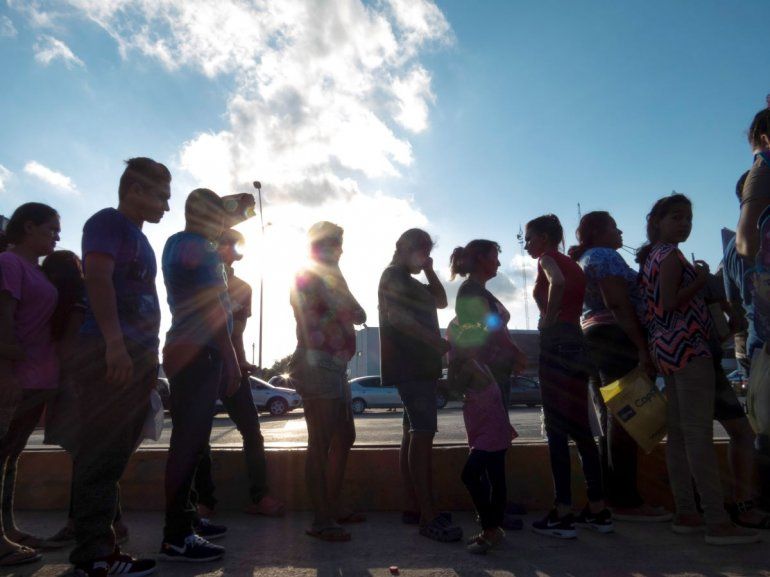 En esta fotografía de archivo del 5 de octubre de 2019, varios migrantes que desean asilo en Estados Unidos hacen fila con sus documentos en el campo para migrantes afuera de El Puente Nuevo, en Matamoros, México. 