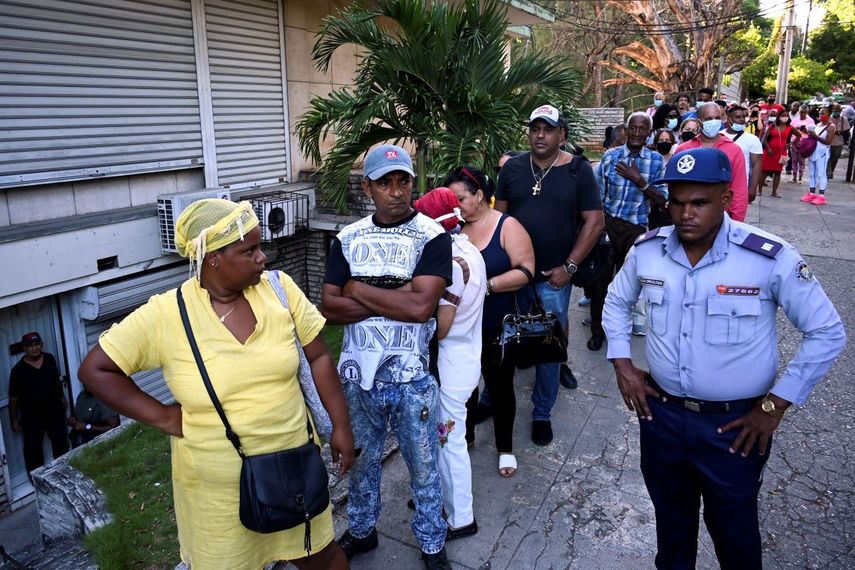 Cubanos hacen fila, bajo la custodia de un agente del régimen.&nbsp;